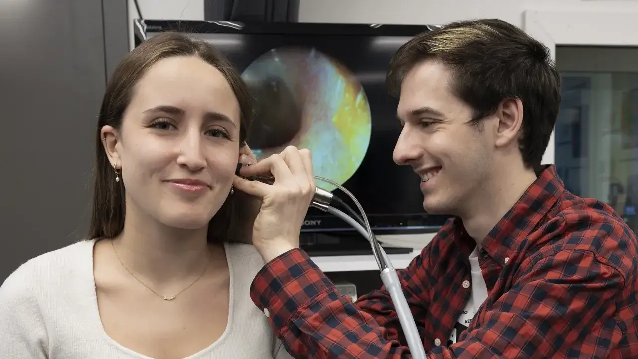 Un &eacute;tudiant en formation audioproth&eacute;siste en Espagne &agrave; distance examine l'oreille d'une patiente, avec une image de l'int&eacute;rieur de l'oreille affich&eacute;e sur un &eacute;cran.