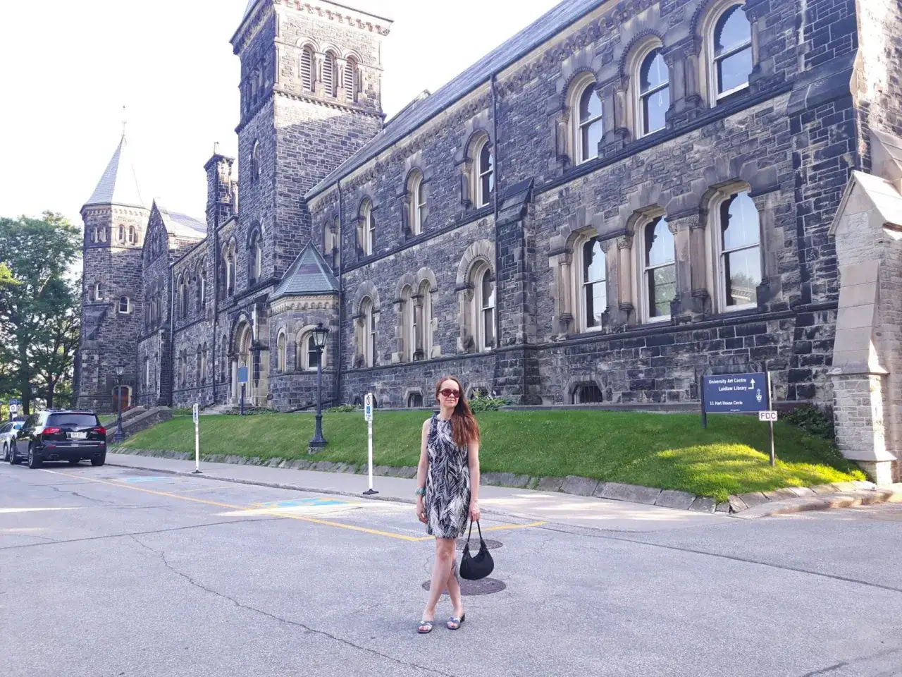 Une femme pose devant l'architecture imposante de l'universit&eacute; de Toronto, un jour ensoleill&eacute;.
