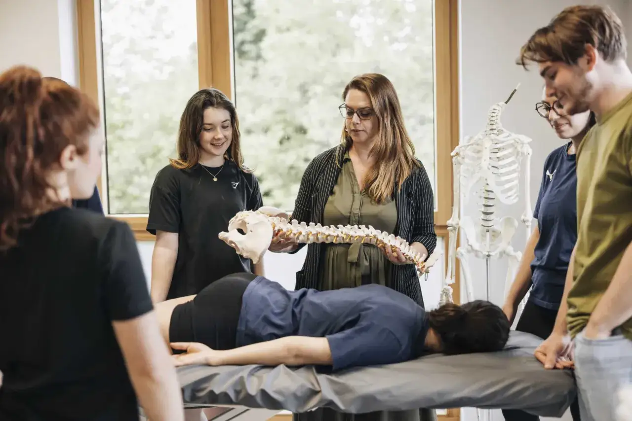 Des étudiants en kinésithérapie au Luxembourg apprennent l'anatomie avec un modèle de colonne vertébrale.