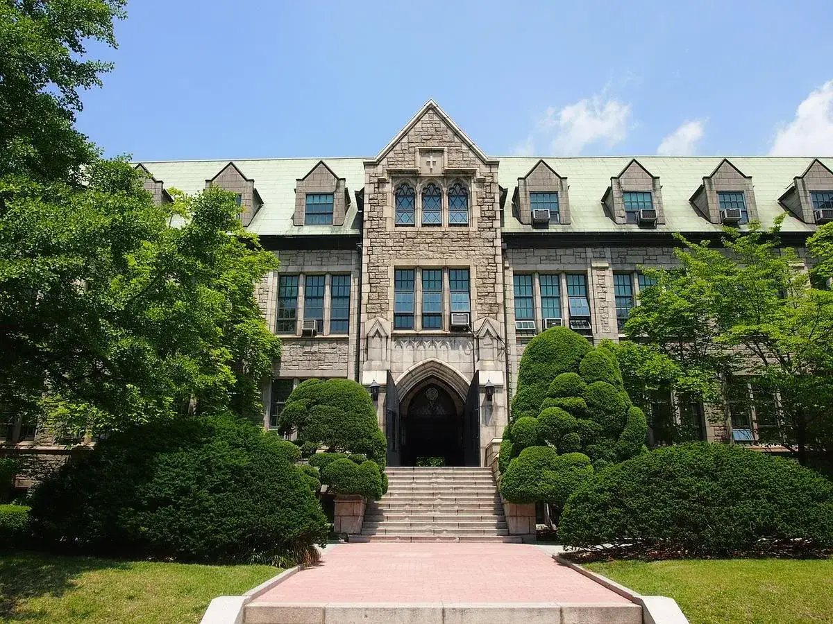B&acirc;timent en pierre de style ancien, avec des arbres verts luxuriants devant. C'est la Korea University Business School.