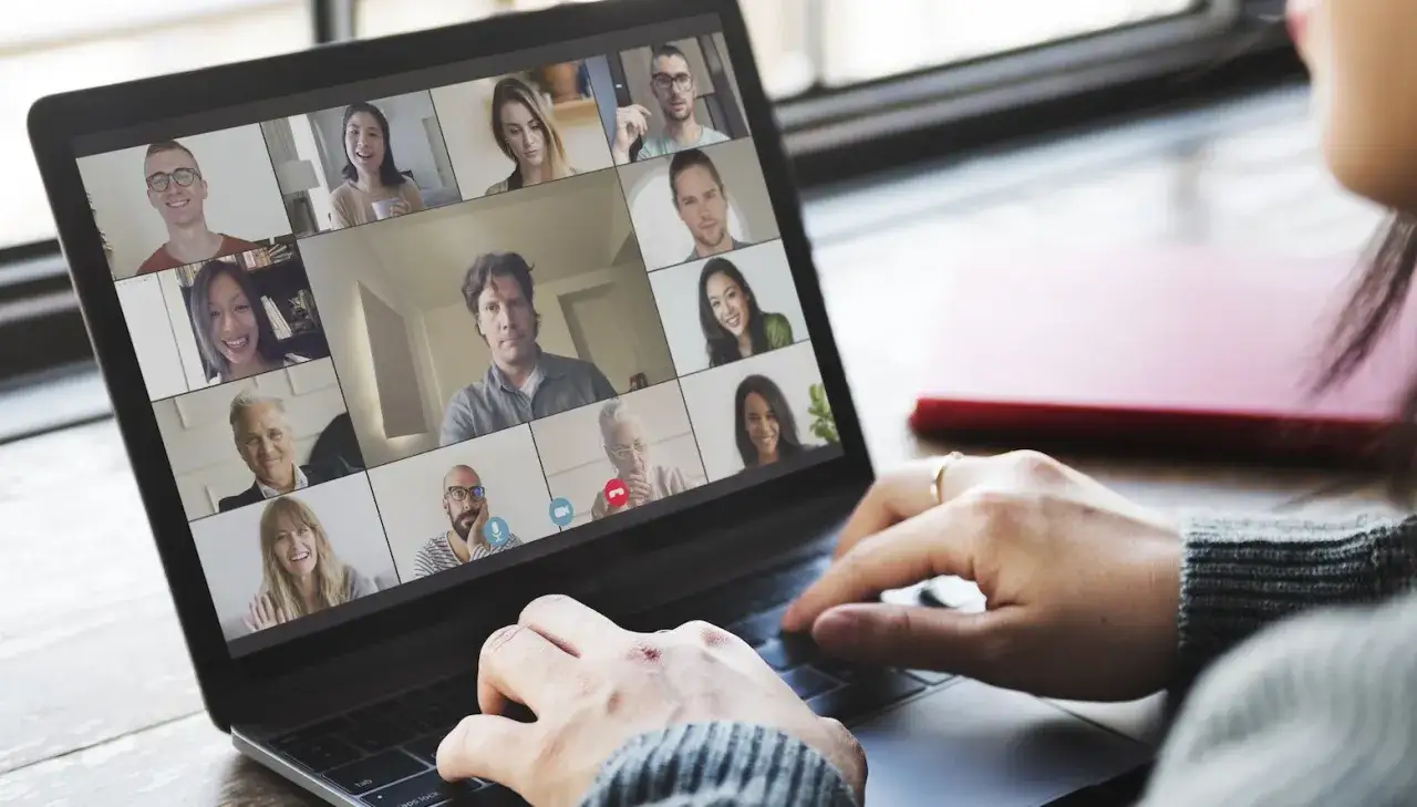 Écran d'ordinateur affichant une visioconférence avec plusieurs participants souriants. Une personne tape sur le clavier, étudiant pour son master économie à distance.