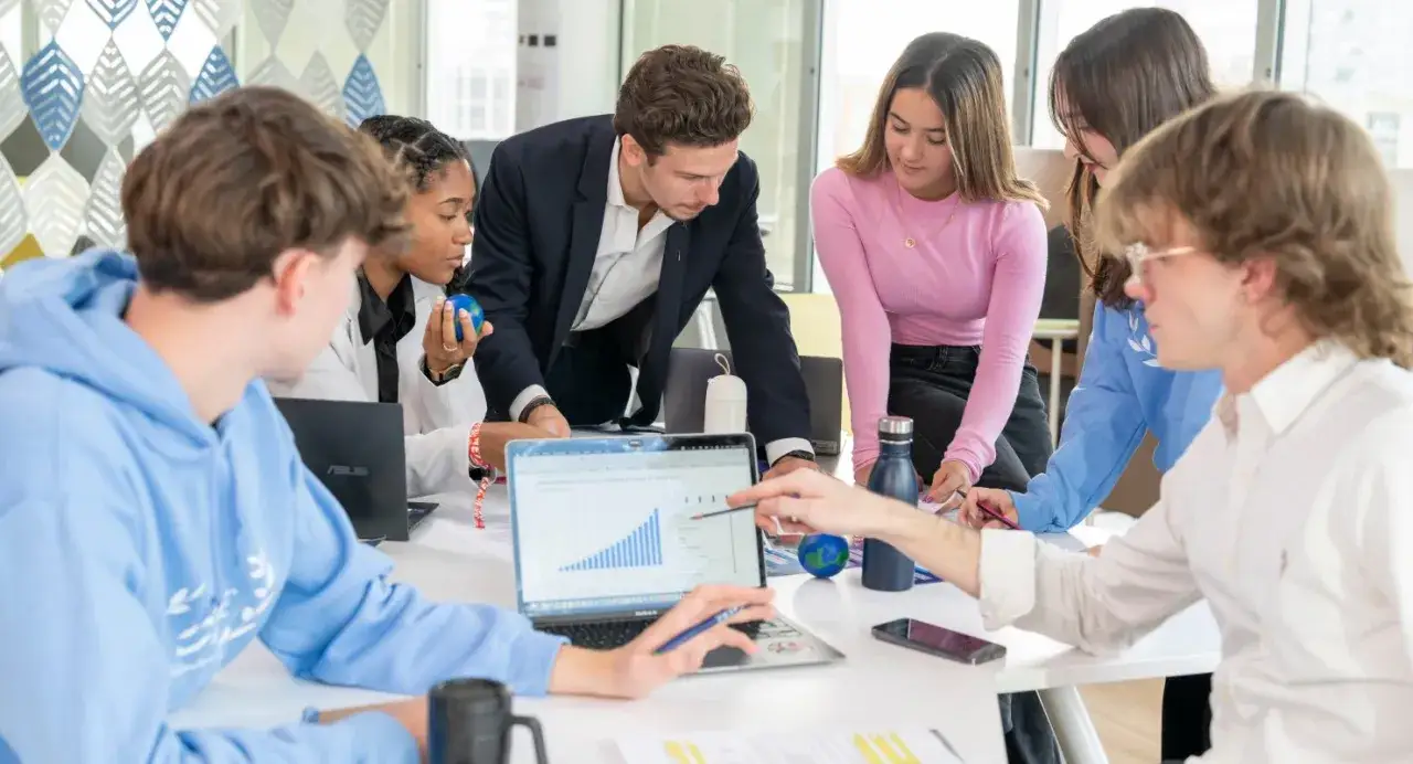 Des étudiants analysent un graphique sur un ordinateur portable, discutant de leur master luxe classement.