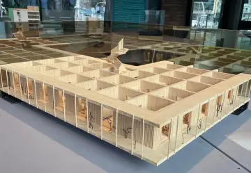 Maquette en bois d'une école d'architecture belge, avec des figures stylisées et des plantes.