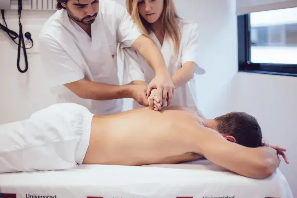 Des étudiants de l'école kine Gérone apprennent la kinésithérapie en pratiquant sur un patient allongé.