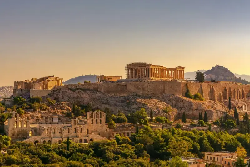 L'Acropole d'Athènes baignée de soleil, un site historique qui rappelle le coût de la vie en Grèce, entre ruines antiques et verdure luxuriante.