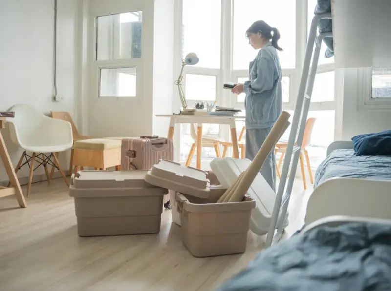 Une jeune femme déballe ses affaires dans une chambre d'étudiant au Canada. Valises et boîtes sont empilées, prête pour une nouvelle vie.